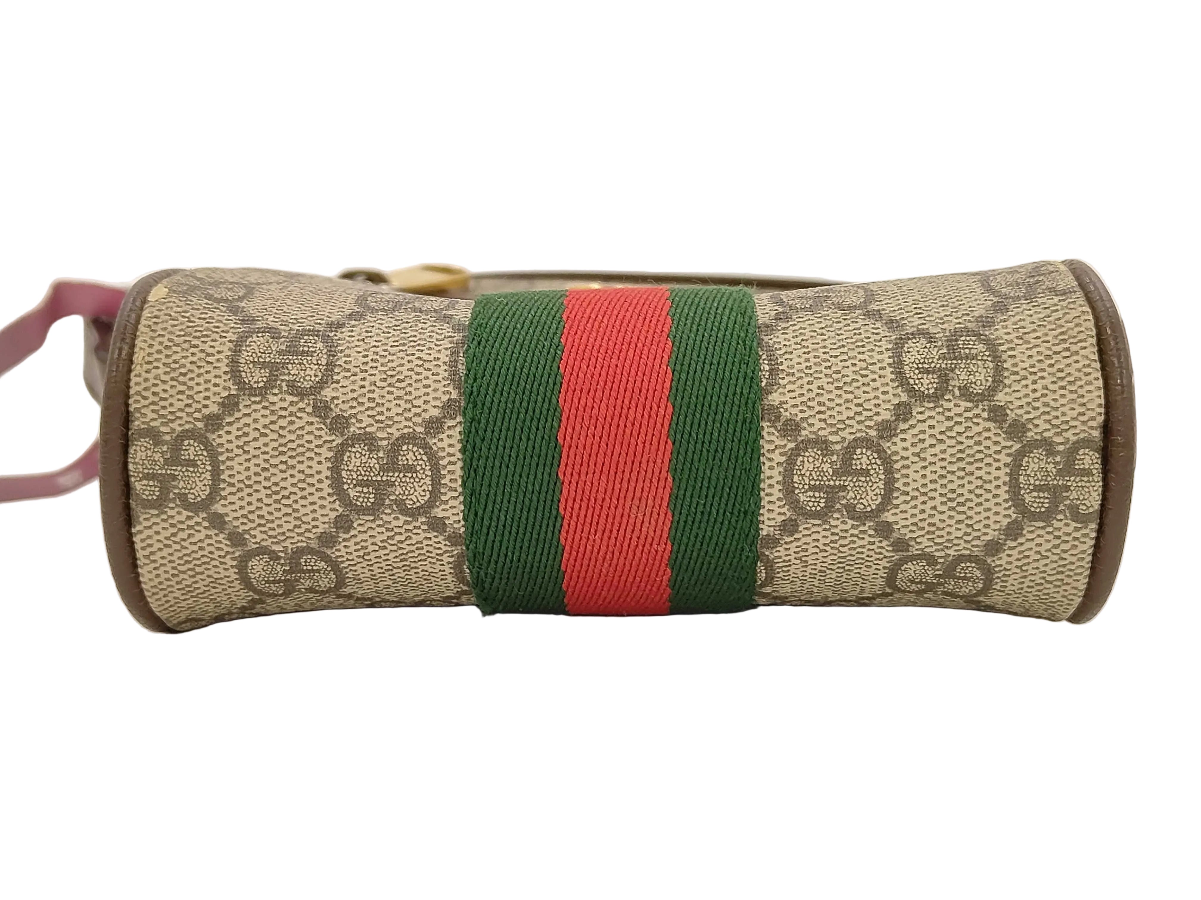 Gucci monogram canvas pouch with a green and red web stripe, brown leather trim, and a pink strap visible on the left, photographed on a white background.