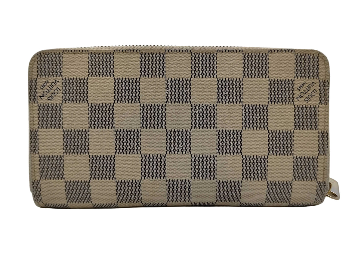 A Louis Vuitton zip-around wallet in the Damier Azur checkered canvas pattern, featuring beige and gray squares with the brand name subtly printed on each square.