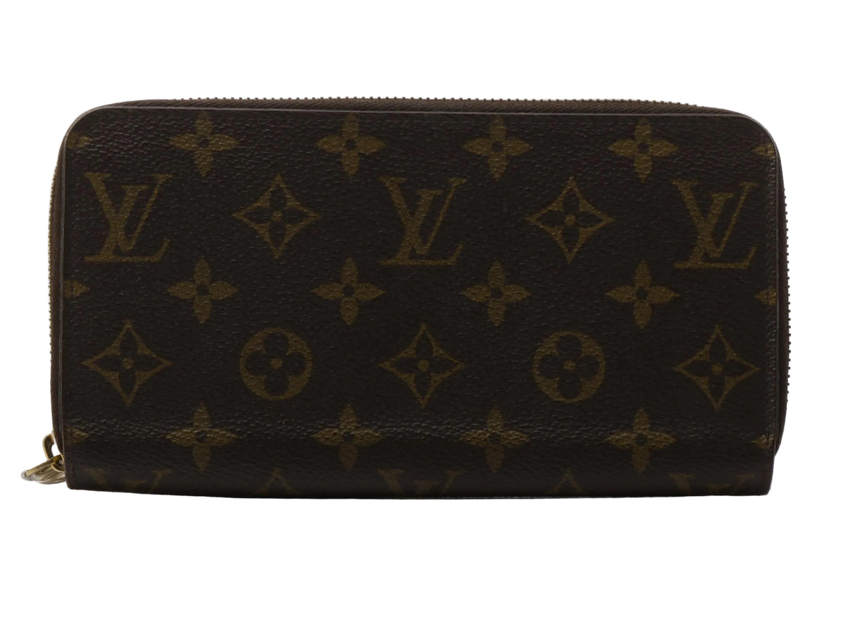 A Louis Vuitton monogram canvas zip-around wallet in dark brown with tan monogram motifs, photographed on a light gray reflective surface.