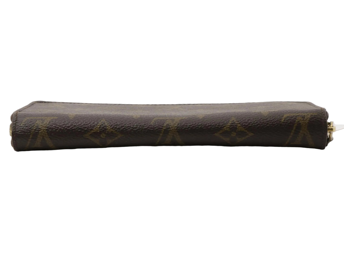 A Louis Vuitton monogram canvas zip-around pouch in dark brown with gold-tone hardware, shown horizontally on a light gray reflective surface.