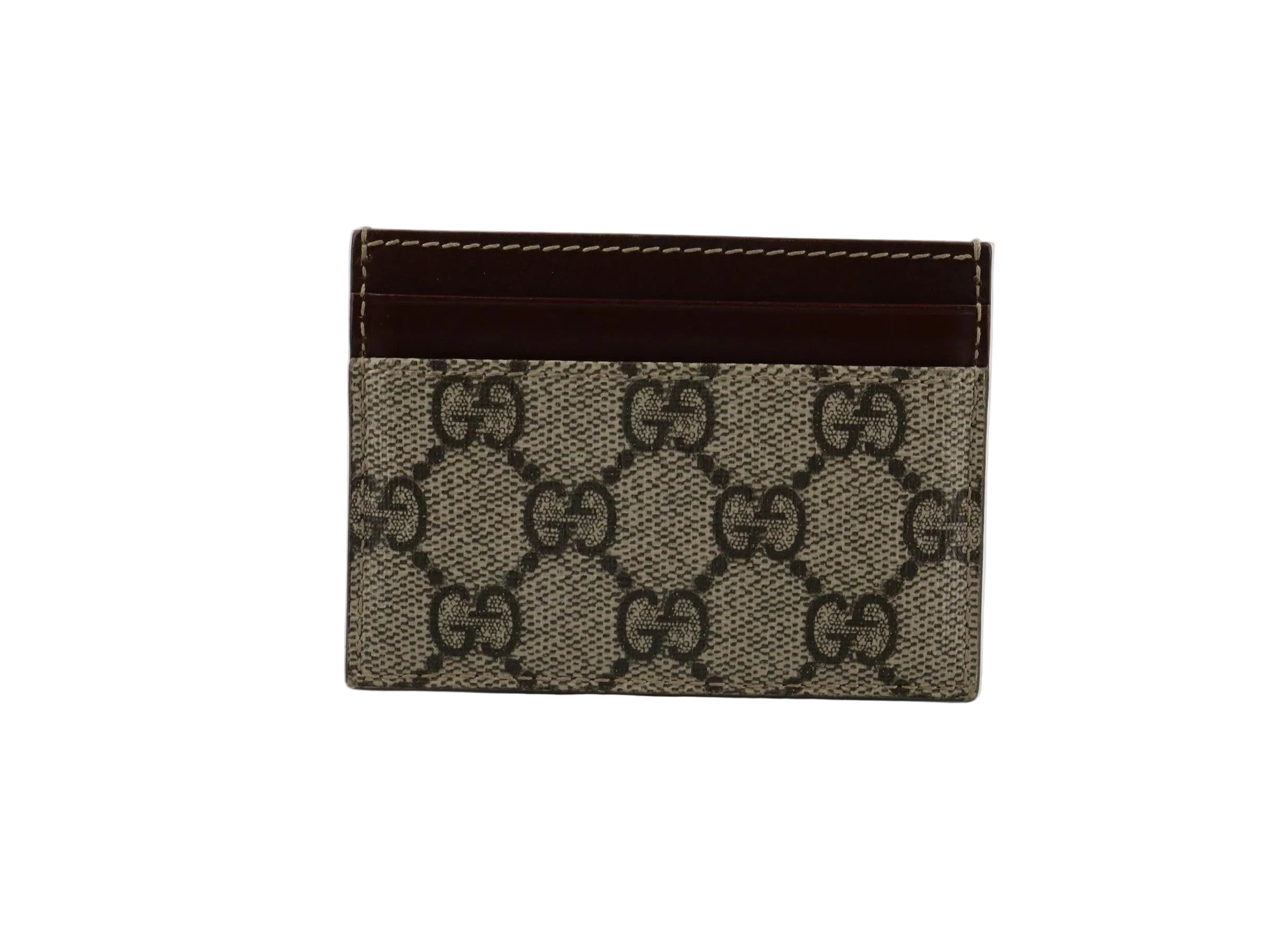 A small Gucci card holder or wallet in the brand's classic GG monogram canvas with a dark brown leather top band, shown on a light gray reflective surface.