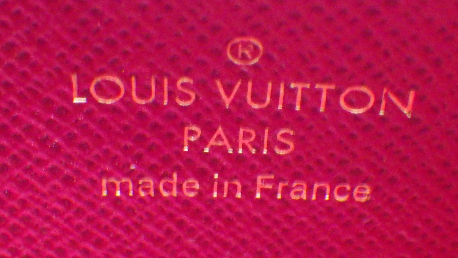 Close-up of a textured pink Louis Vuitton leather surface with embossed gold lettering reading 'LOUIS VUITTON PARIS made in France'.